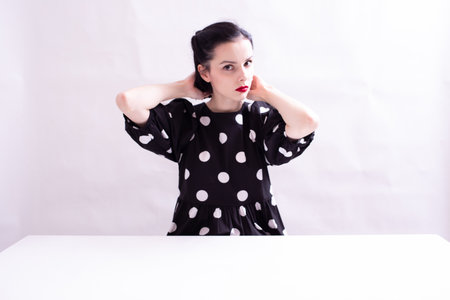 woman in a dress with polka dots with a red mouth sits at a white table, white backgroundの写真素材