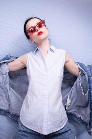 woman in red glasses with red lipstick on her lips in blue clothes on a blue backgroundの写真素材