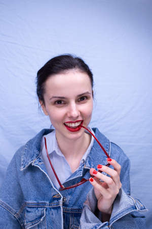 joyful woman with red sunglasses in denim jacket on blue background