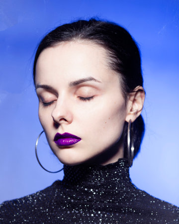 woman with closed eyes in a black turtleneck with sequins on a blue background. High quality photoの写真素材