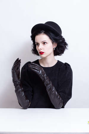 a woman with red lips, curly hair in a black hat and gloves sits at a table. high quality photo