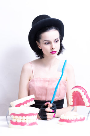 A woman in a dress and hat sits at a table and holds a mock-up of her teeth. high quality photo