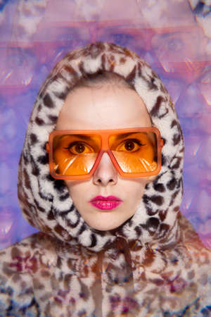 Art portrait, a woman with pink lips in orange glasses and a leopard hoodie on a blue background. high quality photoの写真素材