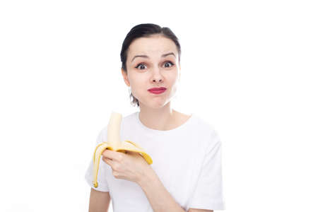 funny woman in white t-shirt eating banana, white studio background. high quality photoの写真素材
