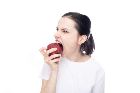 woman in white t-shirt eating red apple, white studio background. high quality photoの写真素材
