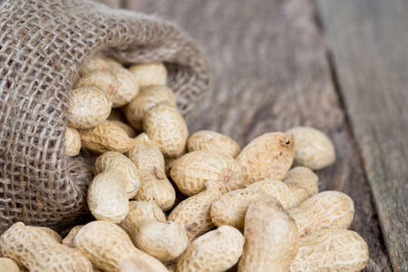 peanuts in a miniature burlap bag on wooden surfaceの写真素材