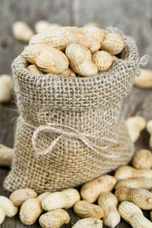 peanuts in a miniature burlap bag on wooden surfaceの写真素材