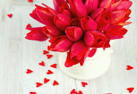 bouquet of red tulips in a pitcher and scattered wooden heartsの写真素材