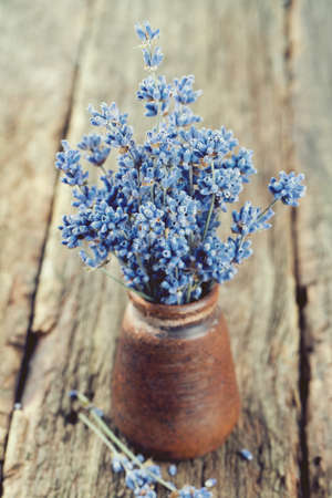 dried lavender in a miniature clay vase on wooden surfaceの写真素材