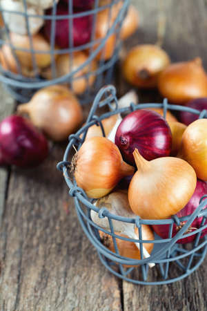 red and yellow onion in an iron basket on wooden surfaceの写真素材