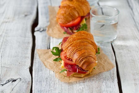 croissants with argugula, jamon, cheese and tomato on wooden surfaceの写真素材