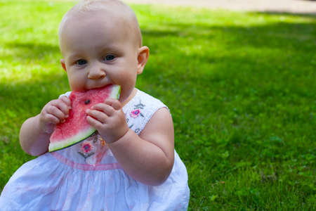 cute baby girl in white dress is eating water melonの写真素材
