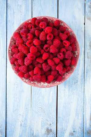 full bowl of raspberries on wooden surface