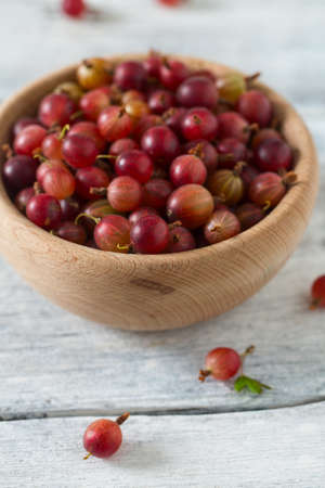 Red gooseberry in a bowl on wooden surfaceの写真素材