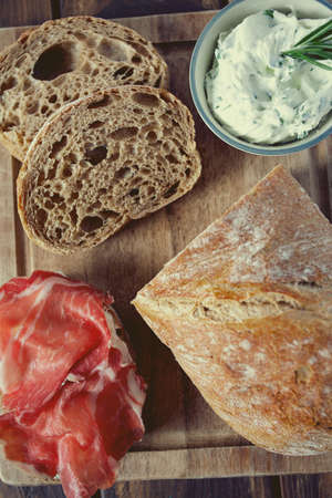 coppa di parma meat, cream cheese and ciabatta bread on wooden surface