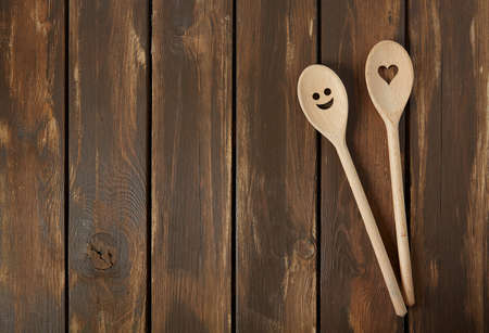 Two wooden spoons on brown wooden surface. Cooking concept. Spoons are with a smile and heart on it.の写真素材
