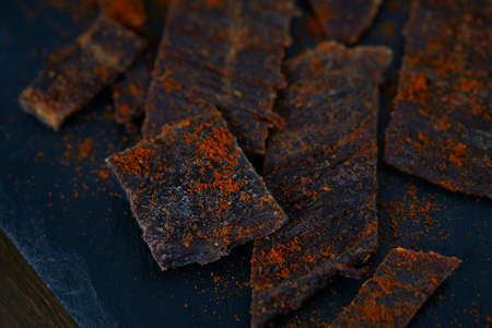Beef jerky with hot pepper on black stone surface. Dried meat.の写真素材