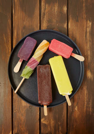 Colorful popsicles on brown wooden surface