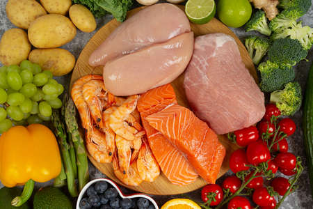 fresh pieces of meat, chicken and salmon and fresh fruits and vegetables arranged around it