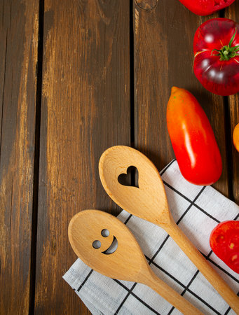 Collection of ripe fresh tomatoes and smiling spoons on brown wooden surface. Cooking and gardening concept. Food backgrounds. Top view.の写真素材