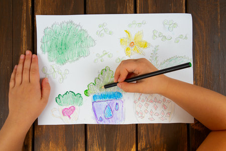 Cute little girl is painting pots with home plants. Top view.の写真素材