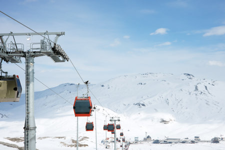 Cable car or ski lift cabins moving against the background of snow-covered mountains and blue sky in the mountain ski resort. Perspective. Winter, Vacation. Extreme sport. Travelの写真素材