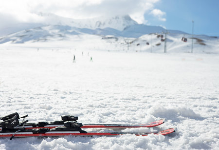 Mountain skis on bright alpine snow against the backdrop of mountains with ski slopes and ski lifts. Winter holidays. Extreme sport. Vacation, travel content. Copy spaceの写真素材