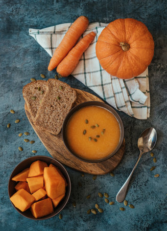 Pumpkin cream soup in a bowl with a spoon on wooden board on the table next to pumpkin whole and cut into pieces. Healthy, vegetarian food. Diet. Home cooking. Thanksgiving dayの写真素材