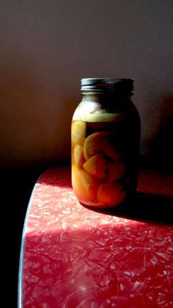 large jar of preserved lemons on a red formica kitchen table in a wedge of sunlightの写真素材