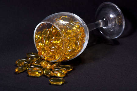 Glass with yellow caplsules of cod-liver oil lying on black backgroundの写真素材