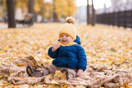happy little boy in the sun in autumn, in the foliage and yellow cute hat holding a leaf