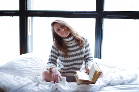 gentle morning of a beautiful girl in sexy lingerie and a sweater lies in bed with a cup and a book. lovely morning moodの写真素材