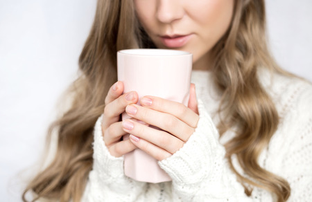 cup in the hands of a girl in a sweater on a white background. home photo