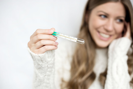 attractive girl in white sweater with thermometer happy recovered. illnessの写真素材