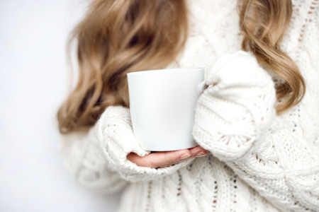 cup in the hands of a girl in a sweater on a white background. home photo