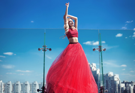 beautiful young girl on the roof of a building in a red lush dress. fashion lookの写真素材