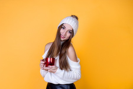 beautiful cheerful happy girl with a cup in a sweater on a bright isolated background of yellow colorの写真素材