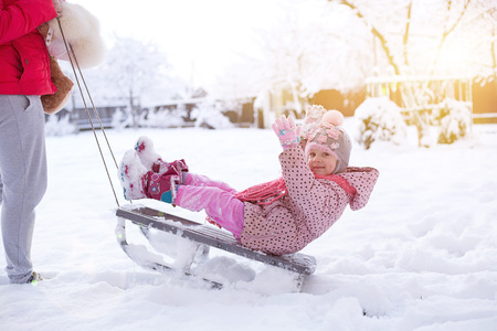 a small child on a sled. girl rolls on snowdrifts in winter, sun shinesの写真素材