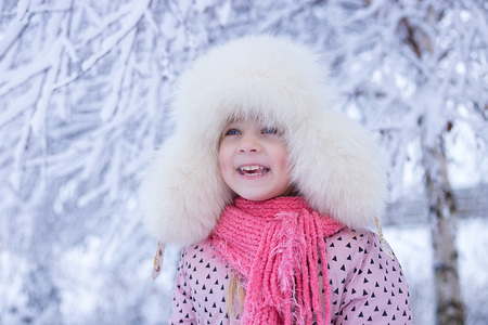portrait of a girl in the winter with the sun in a fur hat. joyful girl, sunny winterの写真素材