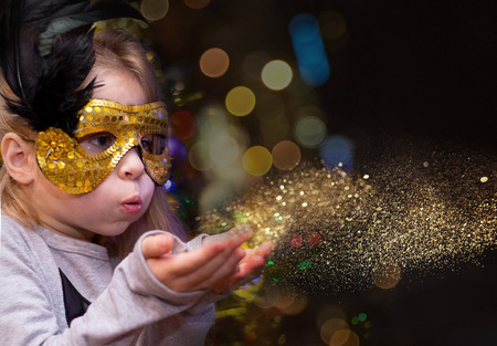 girl blowing golden dust. shine and lights of the night in a carnival mask xmasの写真素材