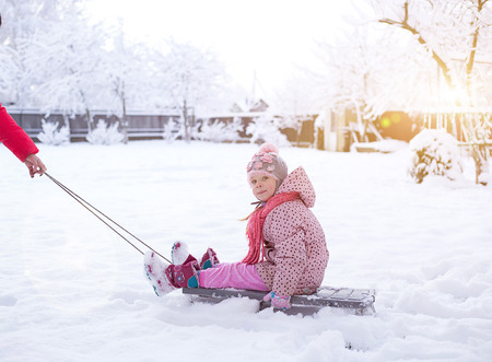 a small child on a sled. girl rolls on snowdrifts in winter, sun shinesの写真素材