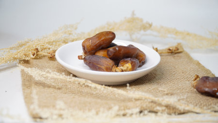Dates fruit in a white bowl on burlap and white background