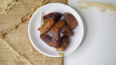Dates fruit on white plate and brown sackcloth on white background
