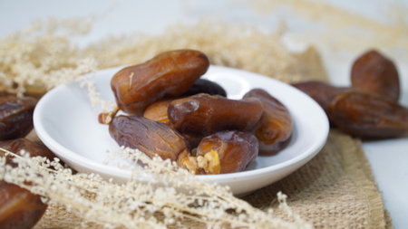 Dates fruit in white bowl with dried grass on wooden background.