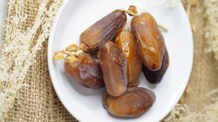 Dates fruit in a white plate on a burlap background.