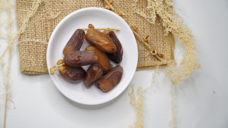 Dates fruit on a white plate on a white wooden background.