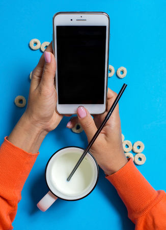 Breakfast with milk in cup and smartphone in hand on blue backgroundの写真素材