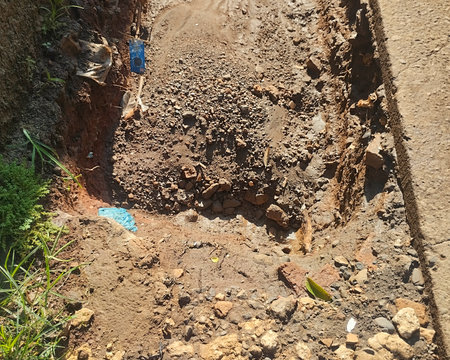 Close-up view of an excavated section of ground showing layers of soil, small rocks, and rough textures under sunlight. The image highlights natural earth composition.の写真素材