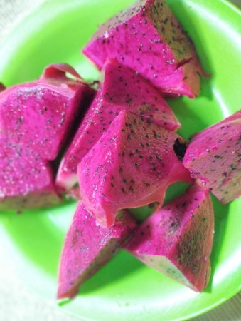 A vibrant close-up shot featuring several wedges of freshly sliced red dragon fruit (also known as pitaya or pitahaya). The fruit displays an intensely bright, magenta-pink fleshの写真素材