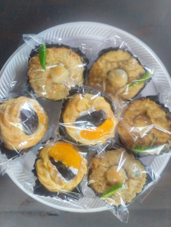 A close-up top view of assorted Indonesian pastries neatly arranged on a white plate and wrapped in clear plastic. The selection includes savory cakes topped with quail eggsの写真素材